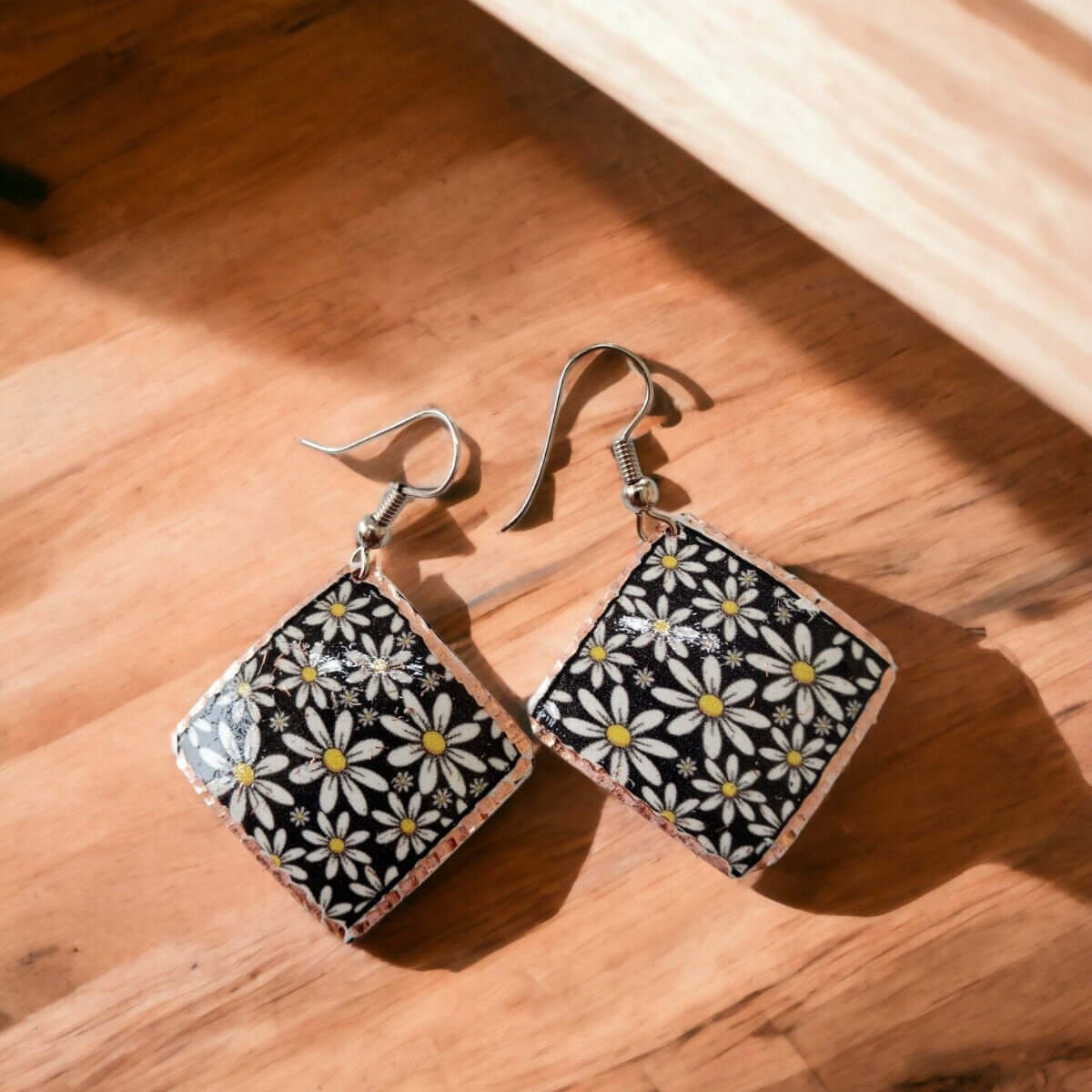 A pair of handcrafted floral daisy copper square earrings laid flat