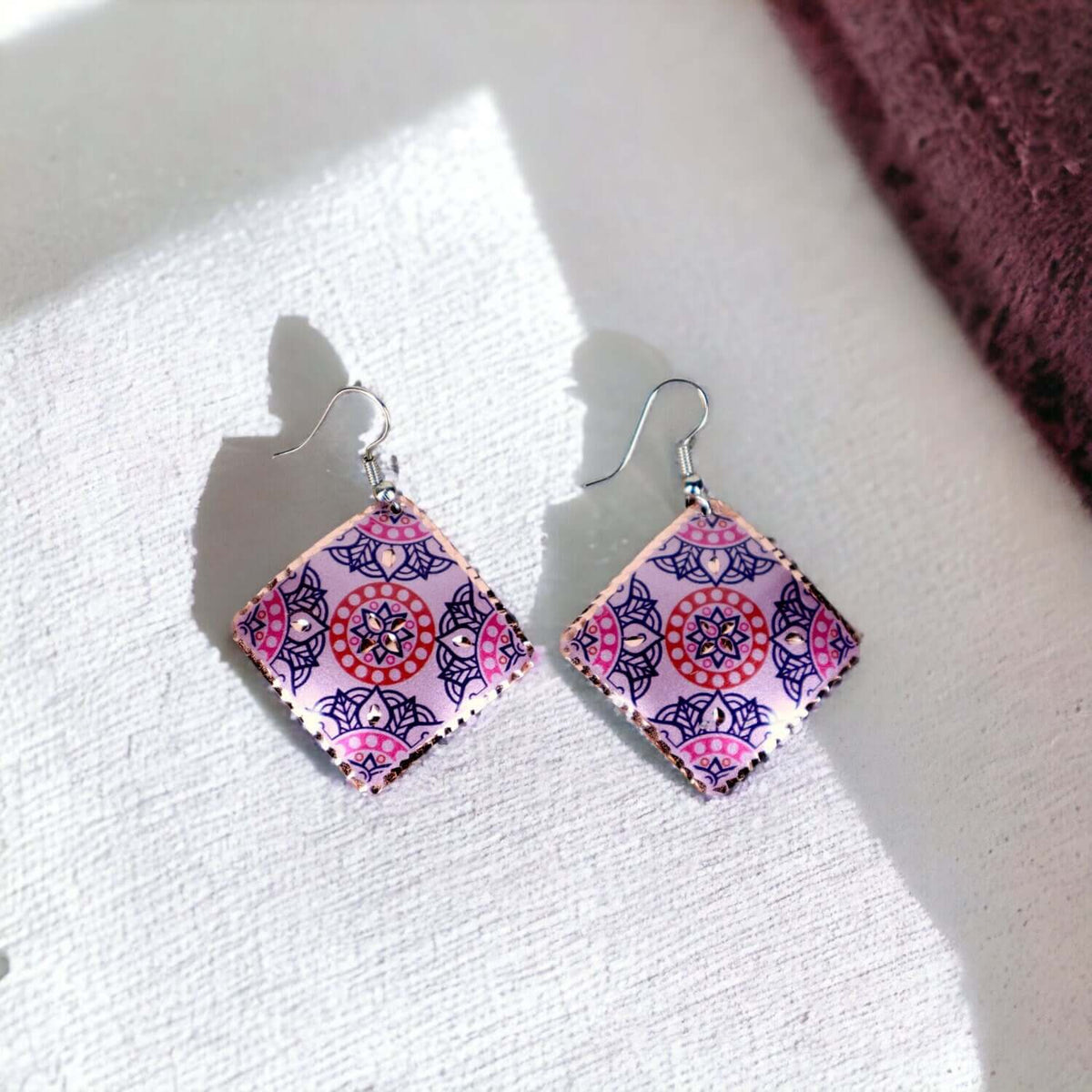 Angled close-up of handcrafted artisan pink copper square earrings