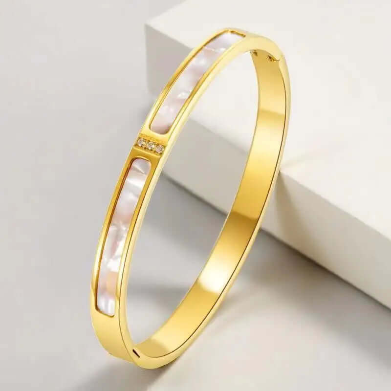 Gold bracelet with a central pearl-like inset on a light background