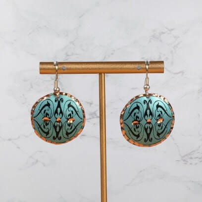A pair of handcrafted artisan green copper circle earrings laid flat
