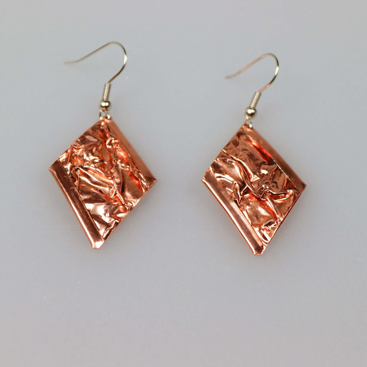 Handcrafted pink wrinkled copper earrings worn on the ear