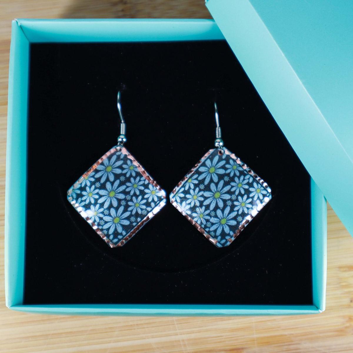 Top-down view of artisan turquoise flower copper square earrings