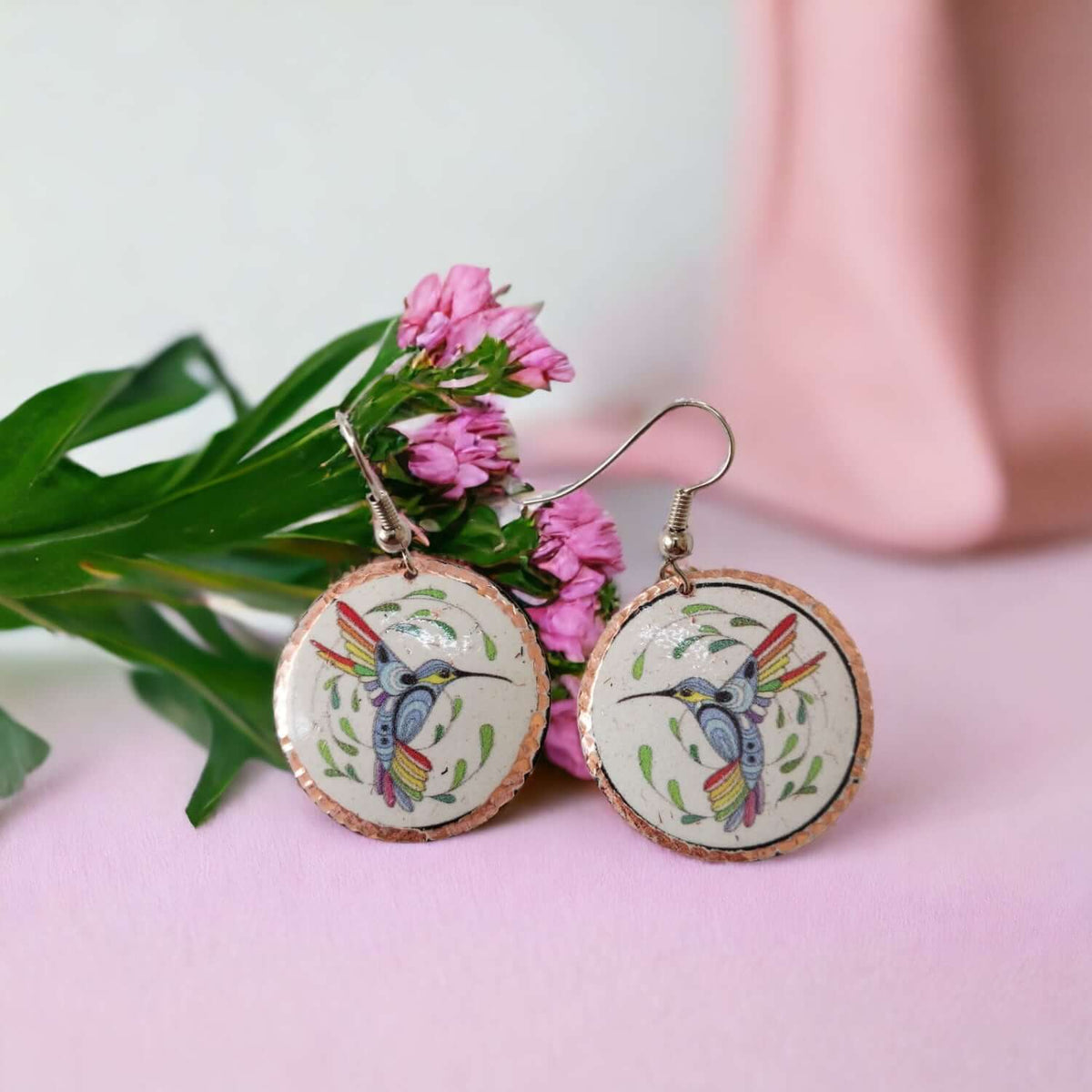 A pair of handcrafted hummingbird copper circle earrings laid flat