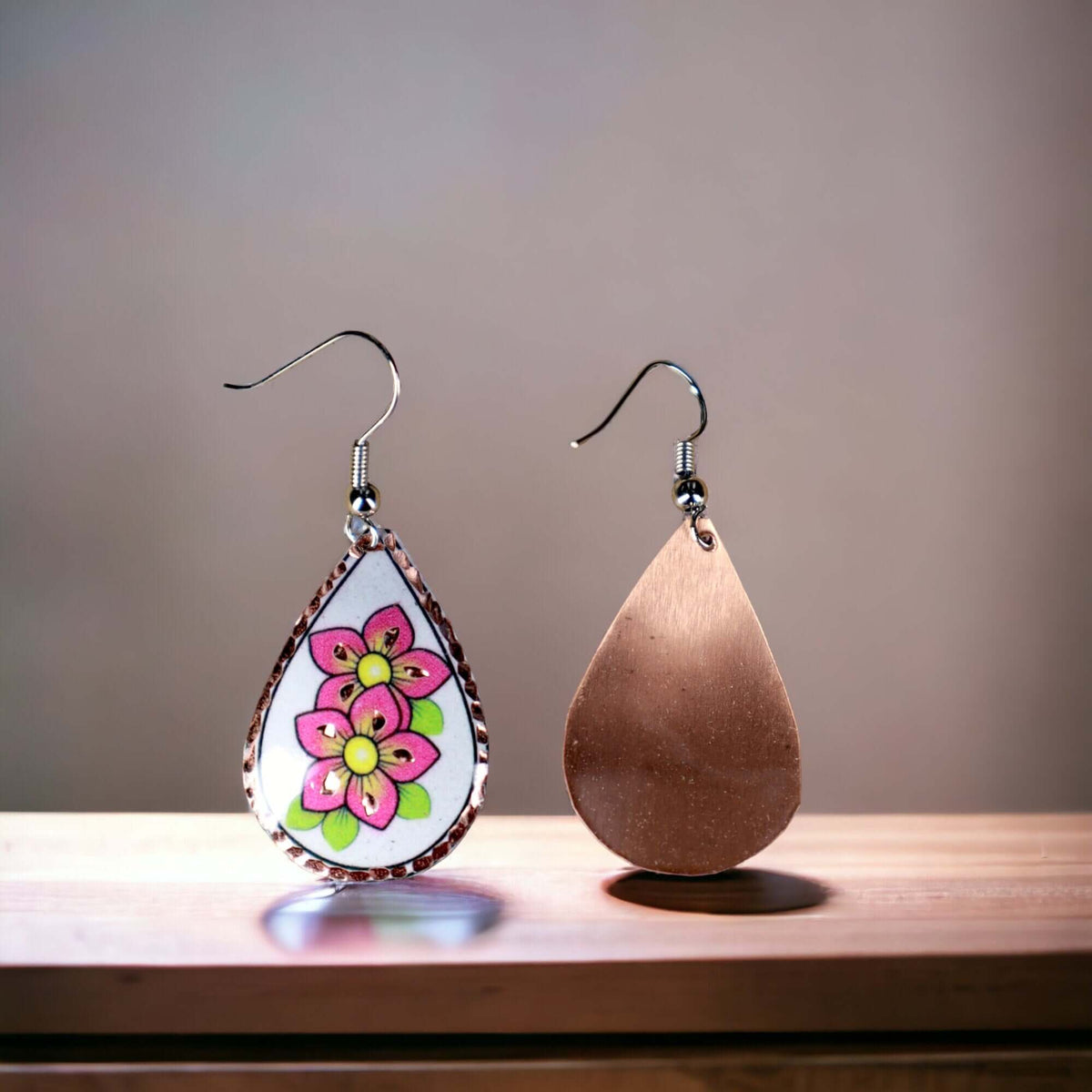 A pair of handcrafted pink flower copper drop earrings laid flat